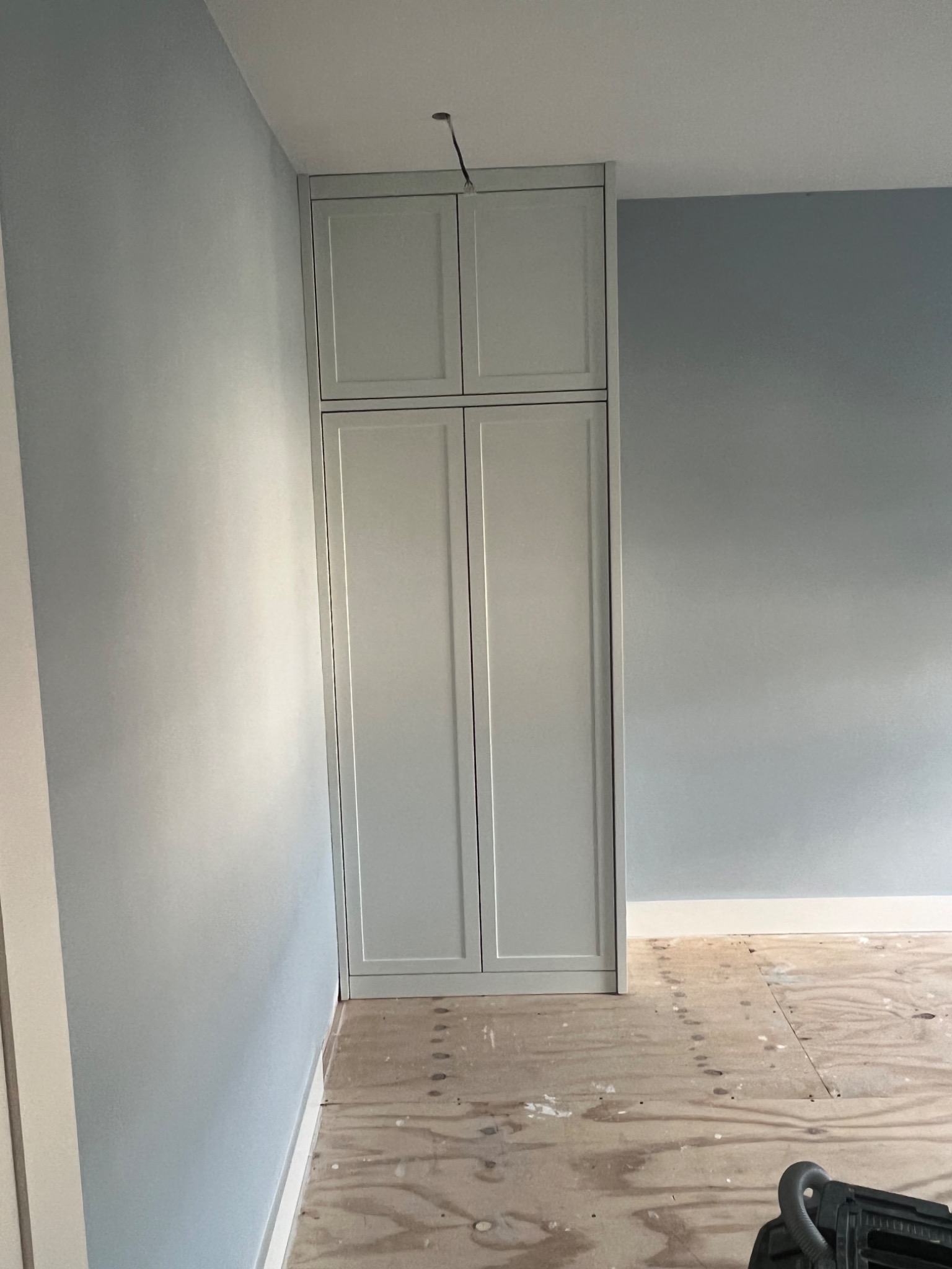 Wbudowana, dwudrzwiowa szafa z nadstawką w jasnym odcieniu szarości, częściowo zamontowana w pokoju z przygotowaną podłogą.