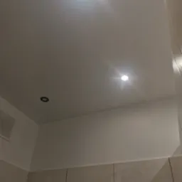 Gładka, biała powierzchnia sufitu z trzema punktowymi źródłami światła LED, widoczny fragment ściany wykończonej płytkami w odcieniach beżu.