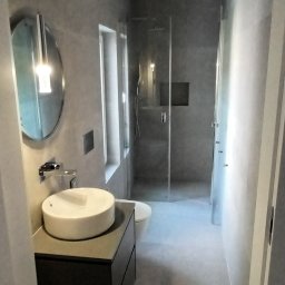 rafhome - Nowoczesna łazienka w odcieniach szarości z okrągłym lustrem, wiszącą umywalką i kabiną prysznicową ze szklanymi drzwiami.