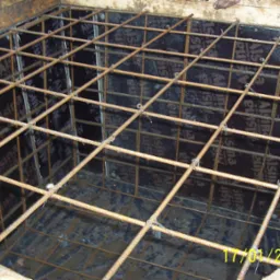 Zbrojenie w szalunku, widok z góry, pręty zbrojeniowe połączone drutem, przygotowane do zalania betonem wewnątrz drewnianej formy.
