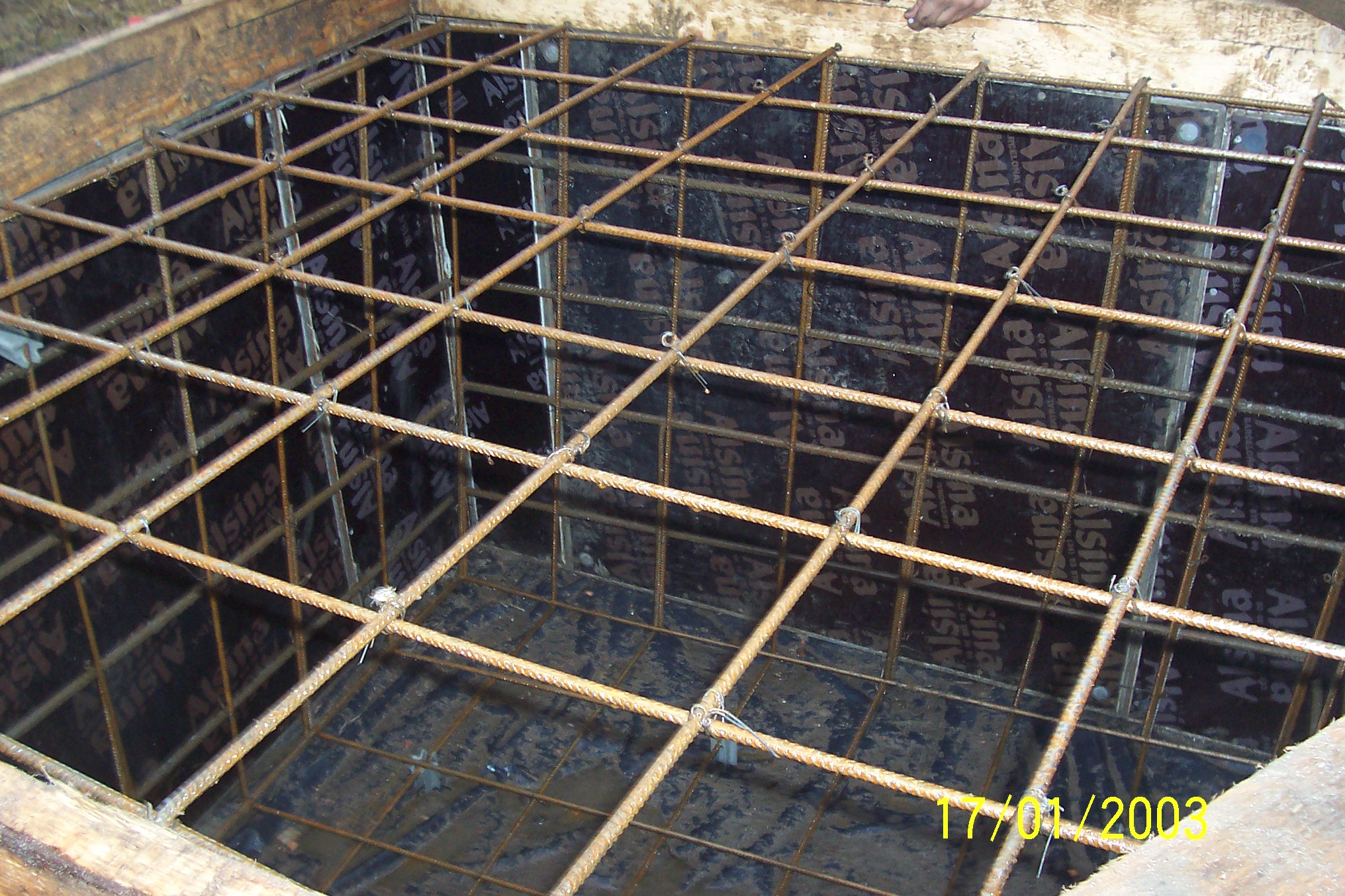 Zbrojenie w szalunku, widok z góry, pręty zbrojeniowe połączone drutem, przygotowane do zalania betonem wewnątrz drewnianej formy.