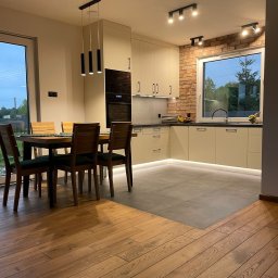 Salon otwarty na kuchnie z cegłą i betonem architektonicznym w połączeniu z waniliowymi szafkami, tworzy kontrast między surowością a ciepłem.
Kolor waniliowy może załagodzić wygląd surowych materiałów, dodając przytulności i elegancji do wnętrza.