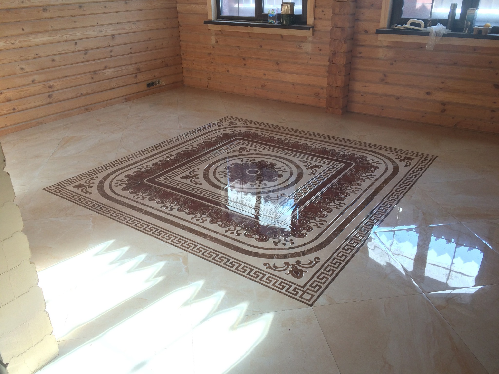 Wykończona podłoga z płytek w drewnianym domu, z ozdobnym wzorem w centralnej części i refleksami światła słonecznego padającego przez okno.