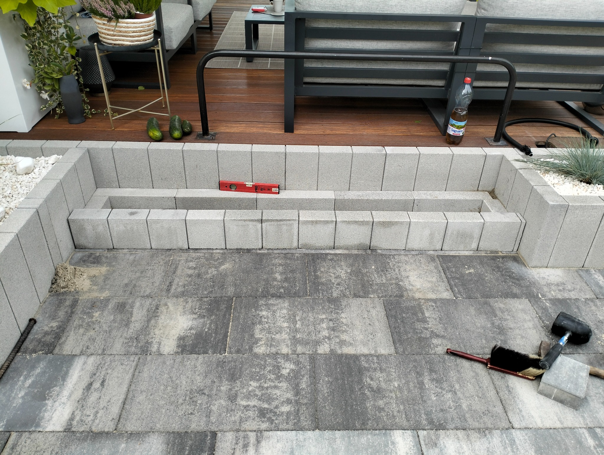 Schody z szarej kostki brukowej w ogrodzie, poziomica na drugim stopniu, na ziemi szczotka i gumowy młotek.