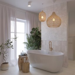 Kreślarnia studio projektowania wnętrz - Jasna łazienka z wolnostojącą wanną, złotą armaturą i rattanowymi lampami, dekorowana roślinami doniczkowymi i drewnianymi stolikami pomocniczymi