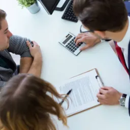 Klient i doradca przy biurku: kalkulator, umowa, podpis, analiza finansowa.