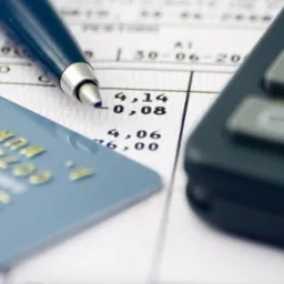 Karta kredytowa leżąca na dokumencie z wyliczeniami, obok kalkulator i długopis.