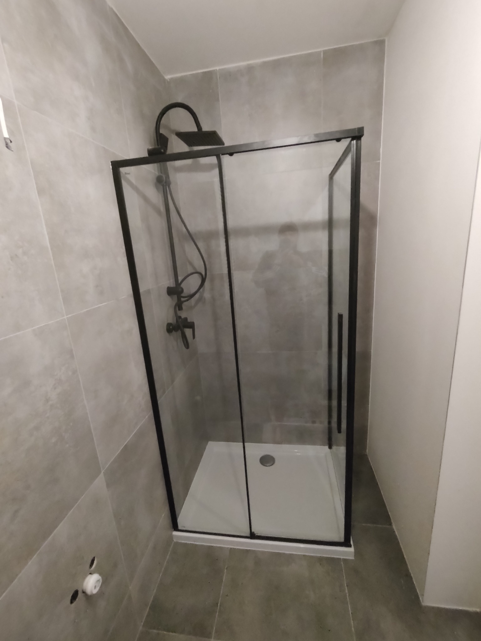 Nowoczesna kabina prysznicowa z czarną armaturą i ramą, szare płytki na ścianach i podłodze, minimalistyczny design.