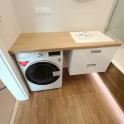 Nowoczesna łazienka z pralką pod blatem drewnianym, umywalką z szafką i oświetleniem podłogowym LED.