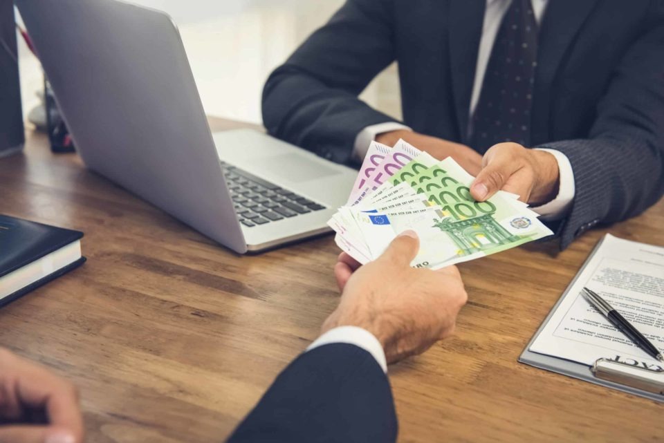 Wręczenie pliku banknotów euro (100 i 200) przy biurku z laptopem i umową, w trakcie spotkania biznesowego.