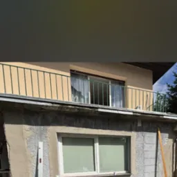 Ocieplanie elewacji budynku z widocznym styropianem i częściowo nałożonym tynkiem, ukazującym etap prac. Widoczne narzędzia i materiały budowlane.