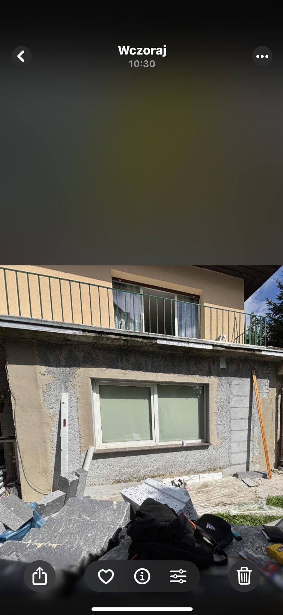 Ocieplanie elewacji budynku z widocznym styropianem i częściowo nałożonym tynkiem, ukazującym etap prac. Widoczne narzędzia i materiały budowlane.