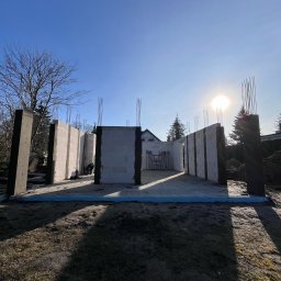Wymurowany Sp. z o.o. - Wznoszenie ścian domu z betonu komórkowego na fundamencie z hydroizolacją w słoneczny dzień, widoczne wystające pręty zbrojeniowe.