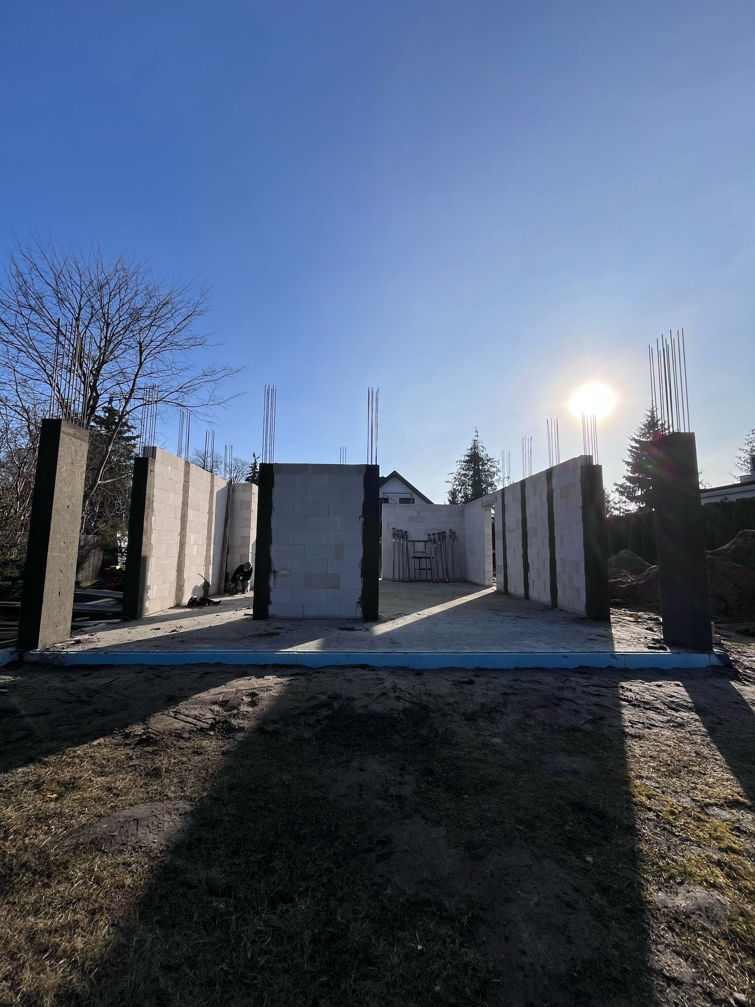 Wznoszenie ścian domu z betonu komórkowego na fundamencie z hydroizolacją w słoneczny dzień, widoczne wystające pręty zbrojeniowe.