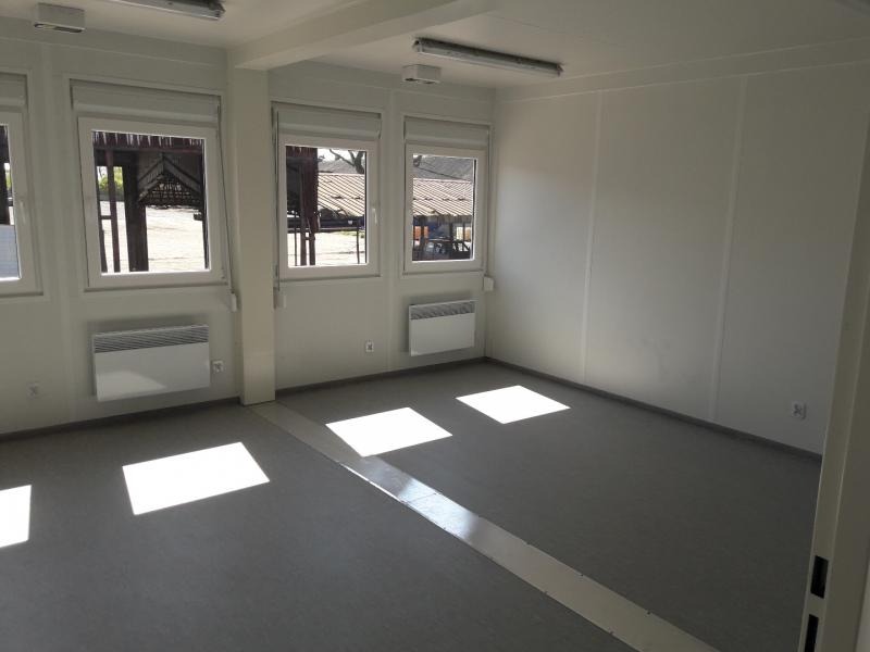 Wnętrze modułowego biura z trzema oknami z roletami, białymi ścianami panelowymi, szarą podłogą i grzejnikami elektrycznymi pod oknami.