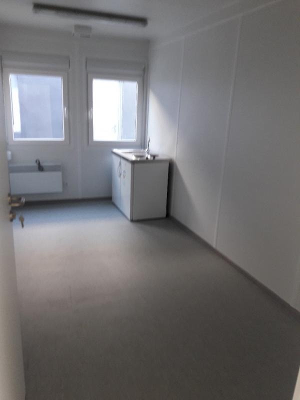 Wnętrze kontenera biurowego z umywalką i oknami, widok na puste pomieszczenie z szarą podłogą i białymi ścianami z paneli.