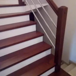 Nowoczesne schody z drewnianymi stopniami w odcieniu ciemnego brązu, białymi podstopnicami i balustradą ze stali nierdzewnej z drewnianym pochwytem.