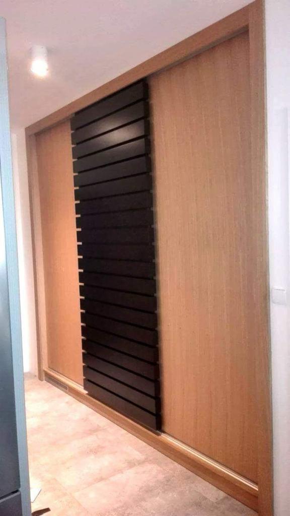 Szafa przesuwna z drewnianymi drzwiami w odcieniach brązu i czarnymi, poziomymi listwami na jednej z części.