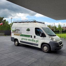 Green Media - architektura krajobrazu - Biały van firmy Green-Media z reklamą architektury krajobrazu, zaparkowany na szarym bruku, z widocznym logo i danymi kontaktowymi. W tle zieleń i polska flaga.
