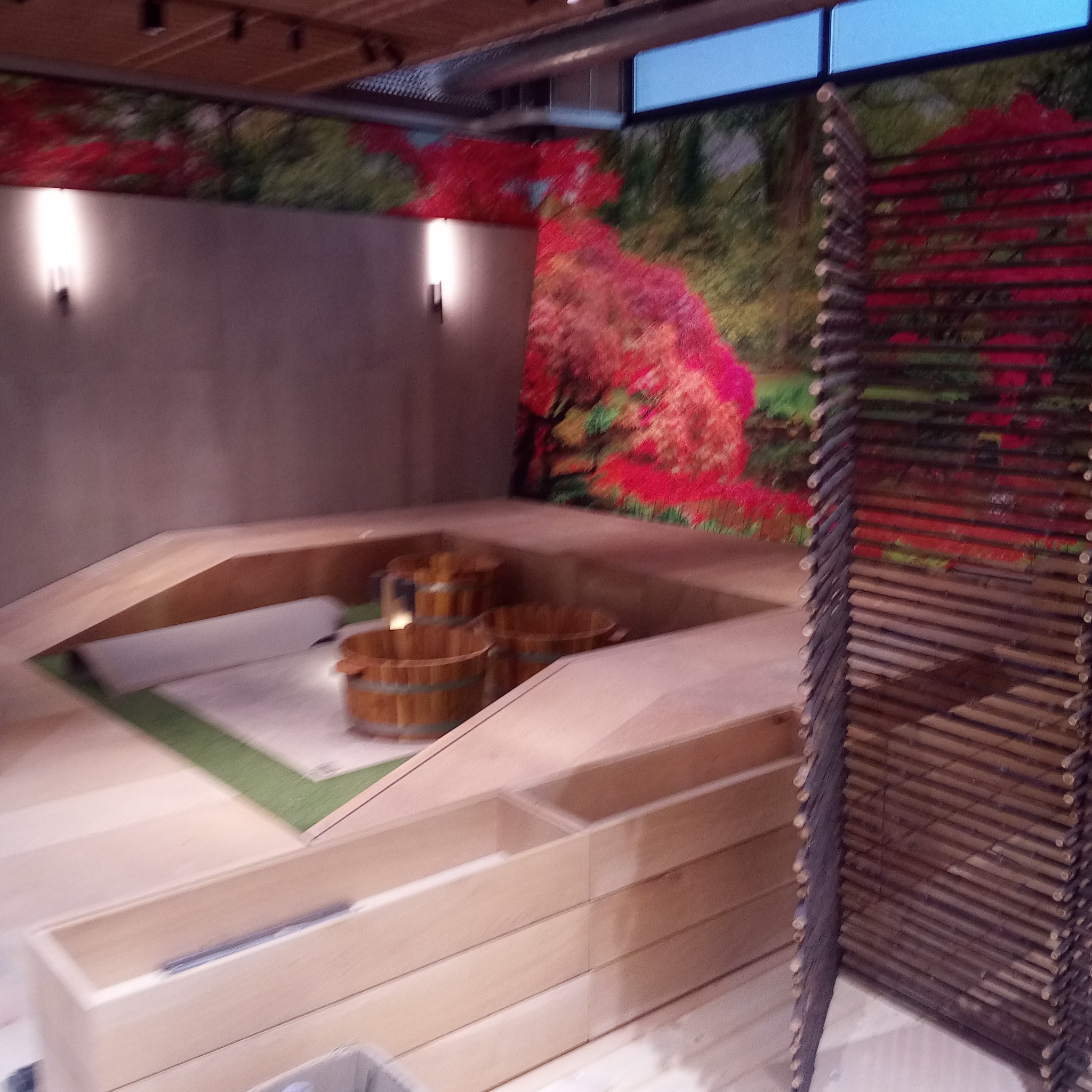 Nowoczesna aranżacja wnętrza z drewnianymi elementami, dekoracyjną ścianą z motywem roślinnym i drewnianymi baliami.