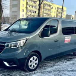 Szary Renault Trafic z naklejką 'Do wynajęcia' na tle miejskiego krajobrazu w zimowej scenerii.