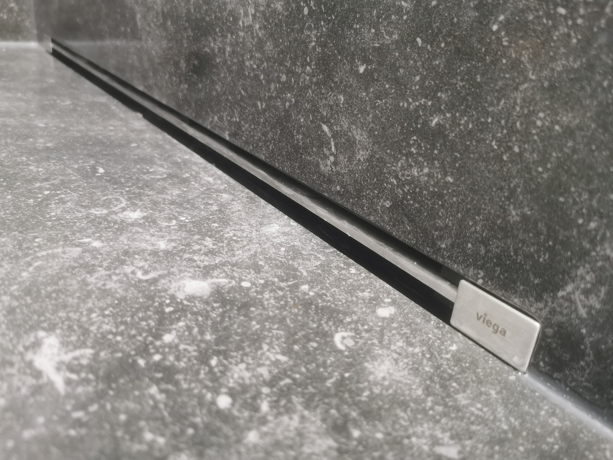 Szczegół odpływu liniowego Viega w posadzce wykończonej szarą płytką w Bukowcu, widoczne zakończenie listwy odpływowej.