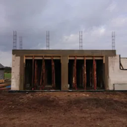 Wznoszenie ścian budynku z betonu komórkowego, widoczne drewniane stemple podtrzymujące nadproże i wystające pręty zbrojeniowe