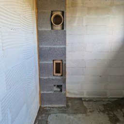 Daniel Gut USŁUGI OGÓLNOBUDOWLANE - Wnętrze w trakcie budowy: ściany z betonu komórkowego, pion instalacyjny z pustaków szarych z widocznym otworem na rurę wentylacyjną i otworem rewizyjnym z drewnianą ramką.