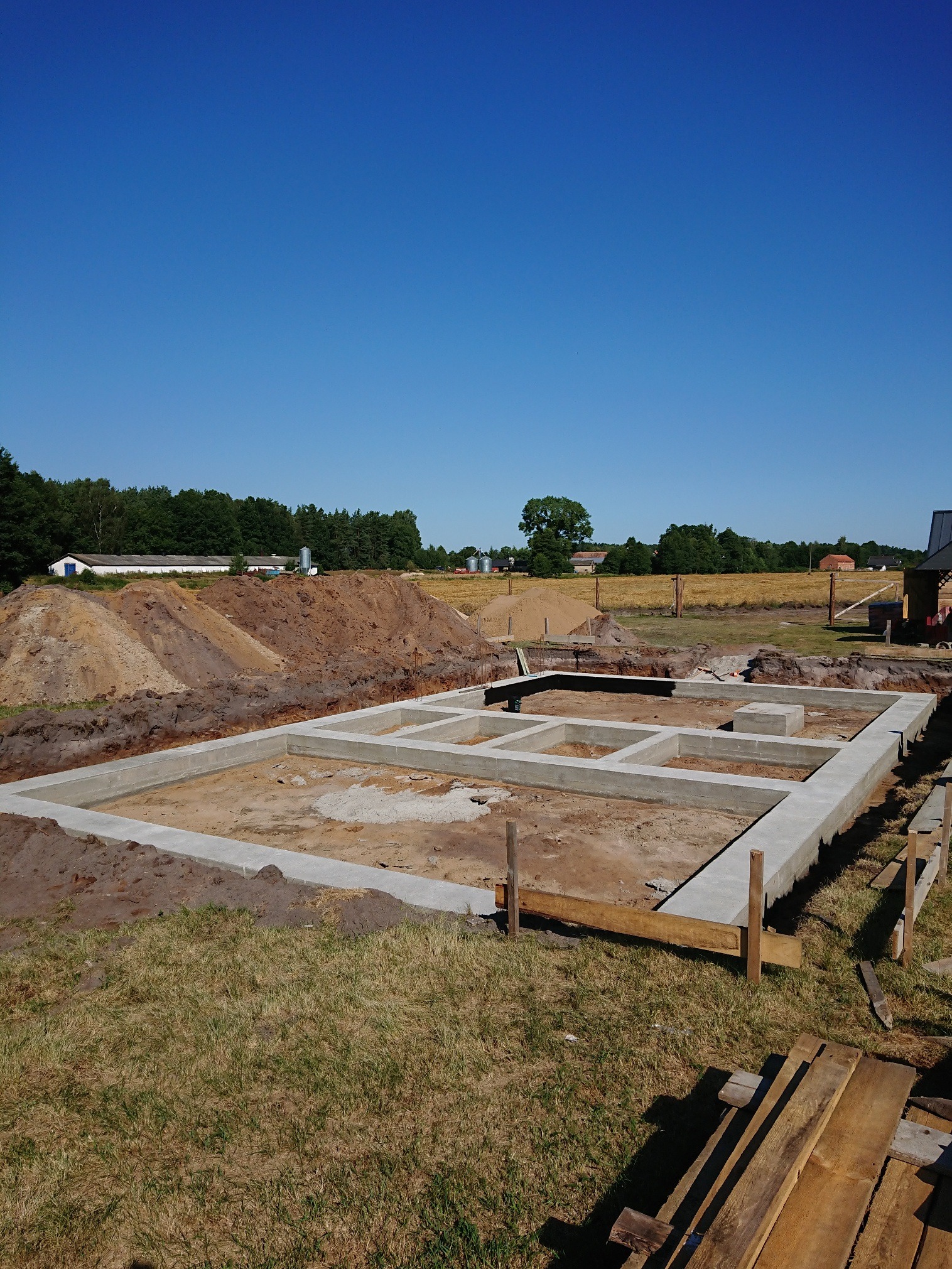 Zalane betonem fundamenty domu jednorodzinnego, widok z góry, w tle wykopana ziemia i błękitne niebo.