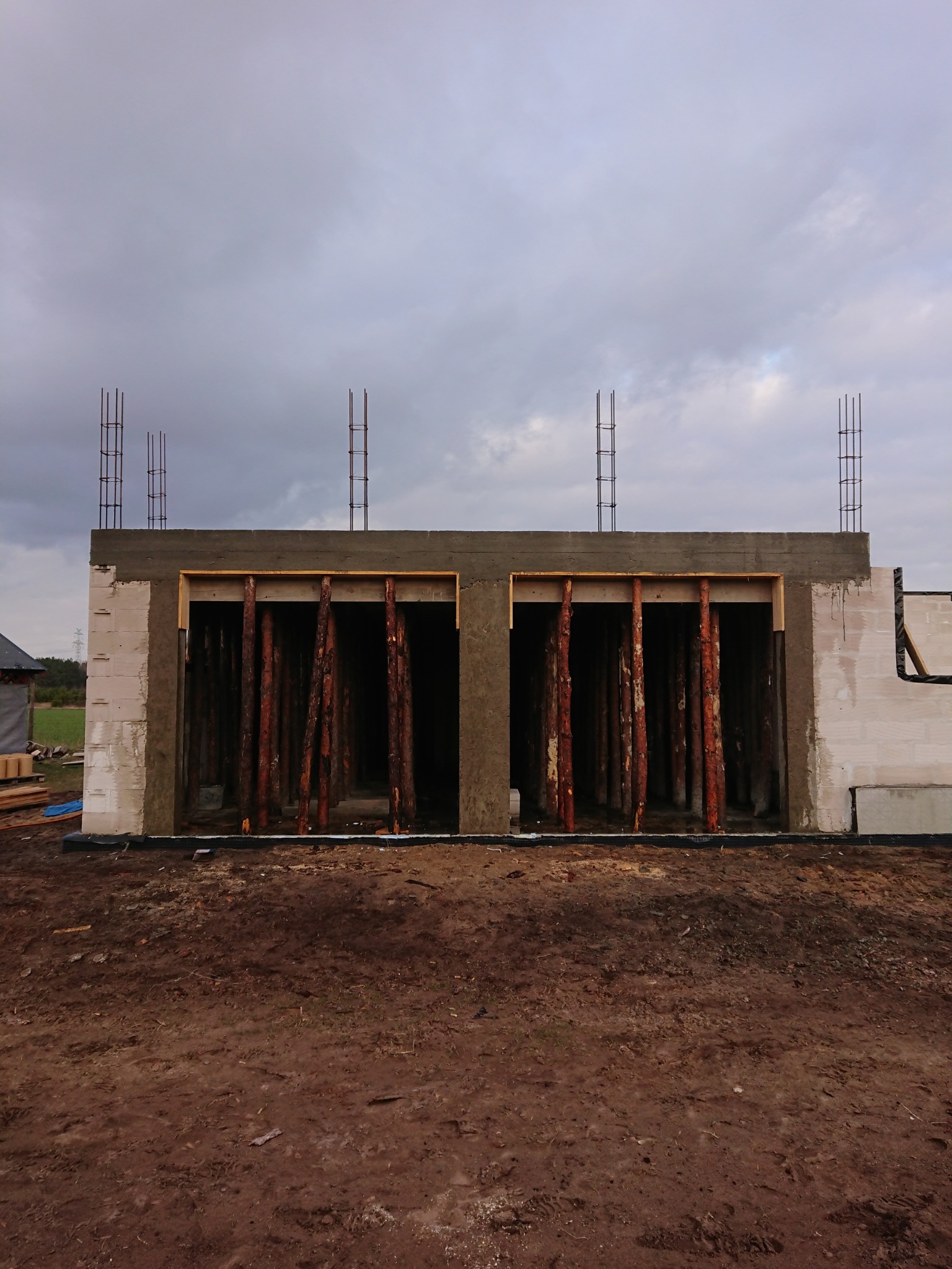 Wznoszenie ścian budynku z betonu komórkowego, widoczne drewniane stemple podtrzymujące nadproże i wystające pręty zbrojeniowe