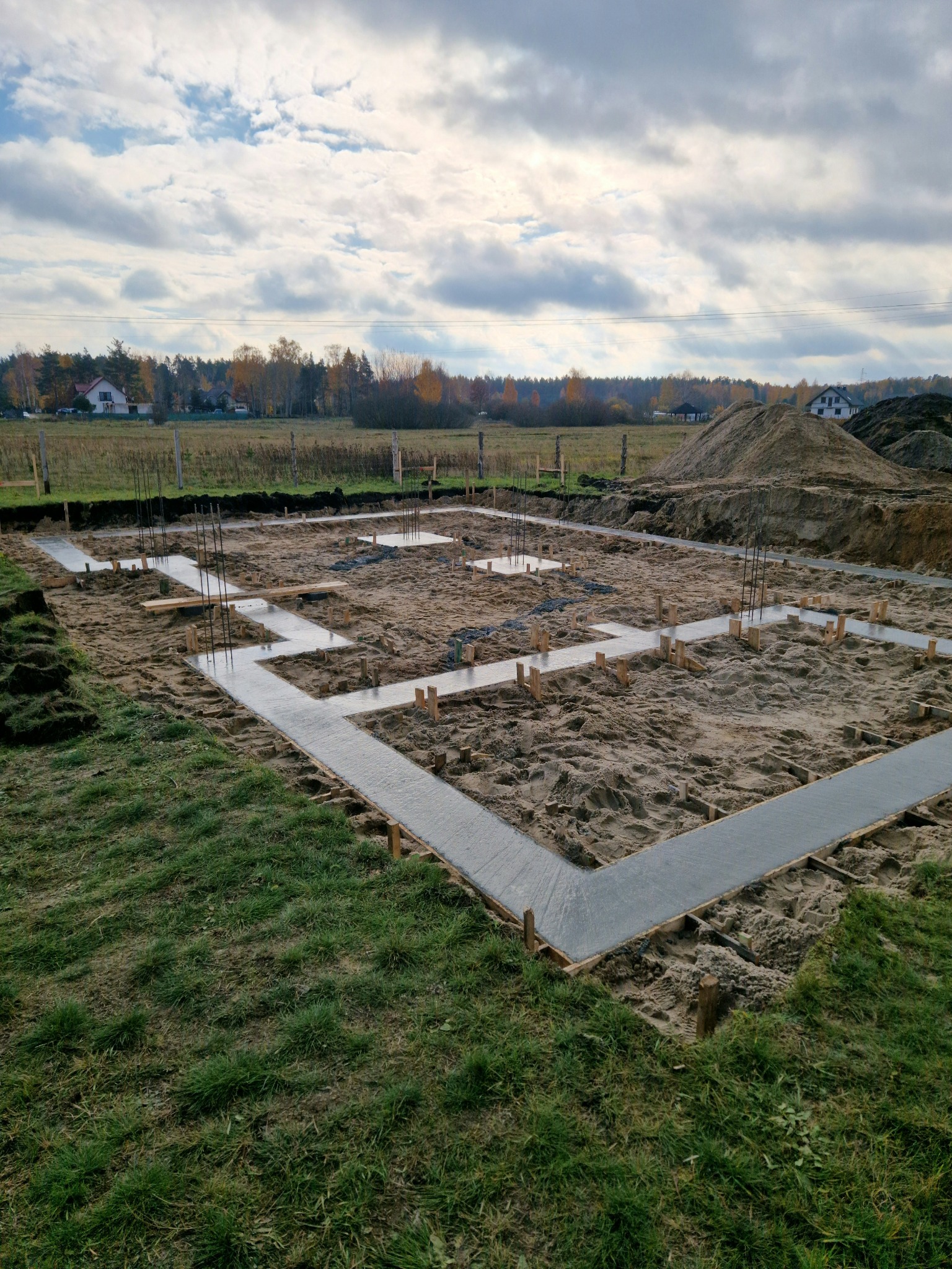 Zalane betonem ławy fundamentowe pod budowę domu w Rudce, widoczne wystające pręty zbrojeniowe i drewniane szalunki.