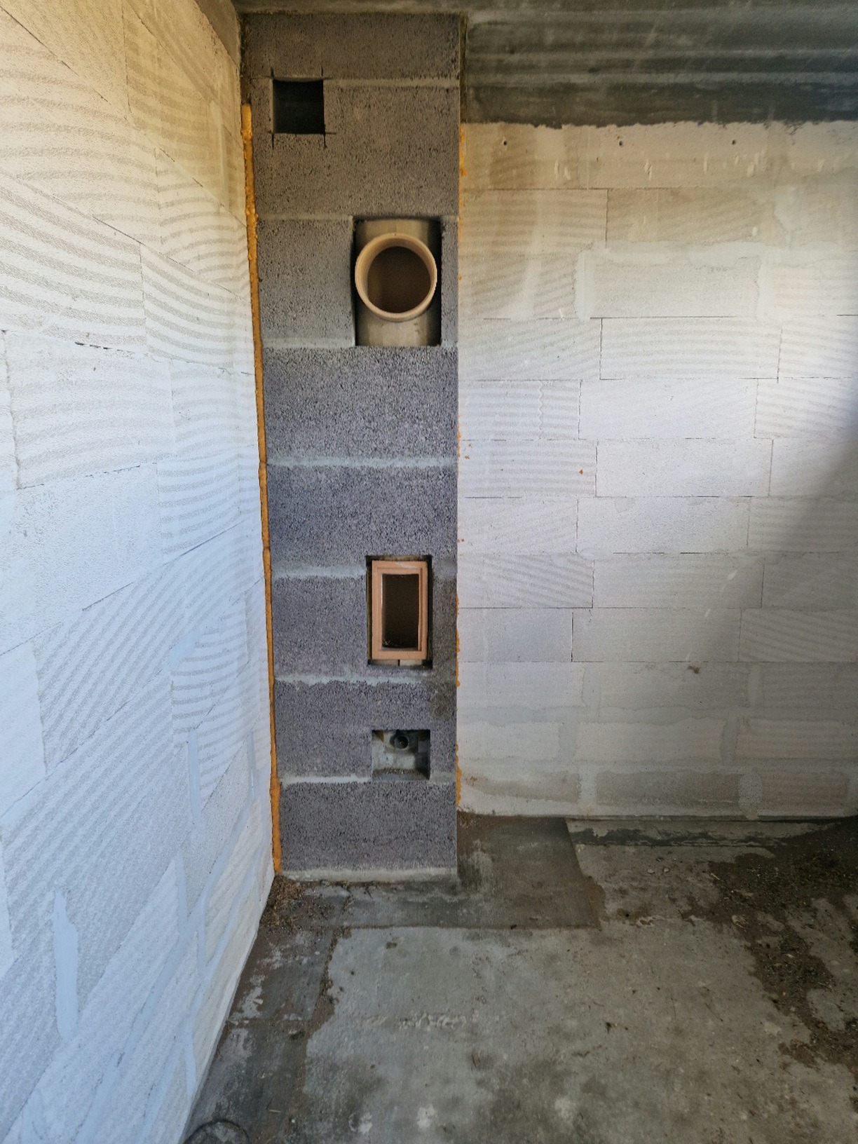 Wnętrze w trakcie budowy: ściany z betonu komórkowego, pion instalacyjny z pustaków szarych z widocznym otworem na rurę wentylacyjną i otworem rewizyjnym z drewnianą ramką.