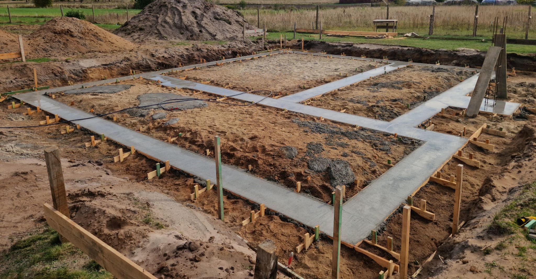 Wylane betonowe ławy fundamentowe z drewnianym szalunkiem, widok z góry na plac budowy w słoneczny dzień.