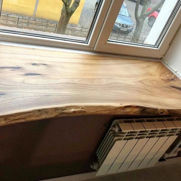 Drewniany parapet z naturalną krawędzią, zamontowany pod oknem, z widocznym grzejnikiem pod spodem.