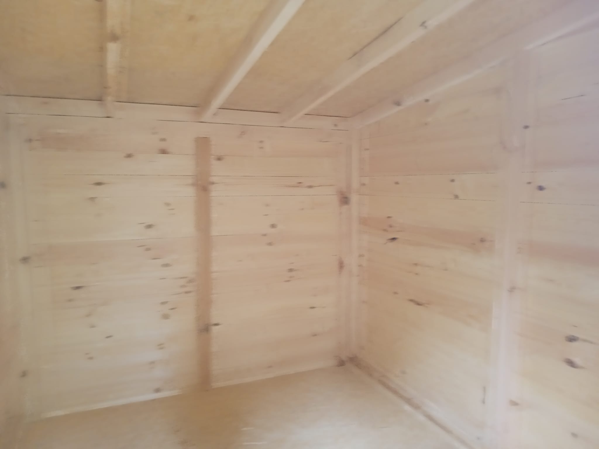 Wnętrze drewnianej konstrukcji z desek, widoczne łączenia i surowe drewno, prawdopodobnie w trakcie montażu.