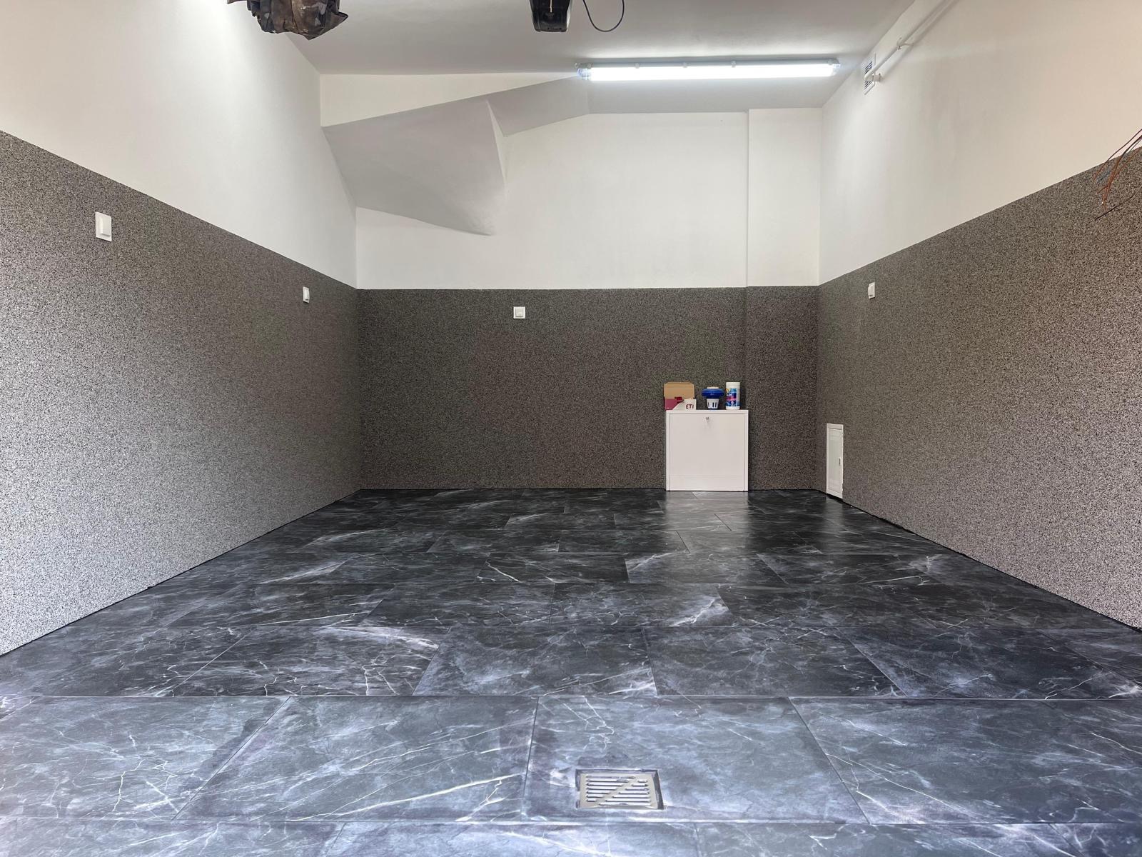 Wnętrze pomieszczenia po remoncie: szara, teksturowana ściana do połowy wysokości, biała góra, podłoga z płytek imitujących marmur, biała szafka z produktami w tle.