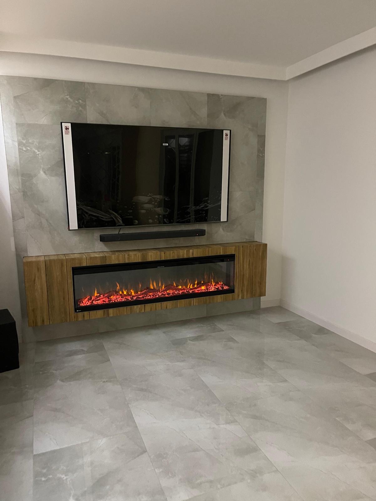 Nowoczesny salon z telewizorem, soundbarem i elektrycznym kominkiem w obudowie z drewnianych paneli na tle ściany z szarych płyt imitujących marmur, podłoga wyłożona płytkami w podobnym odcieniu.