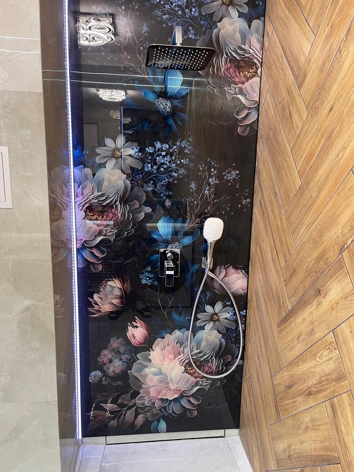 Nowoczesna kabina prysznicowa z czarnym panelem dekoracyjnym w kwiaty, chromowana armatura i drewnopodobne płytki ułożone w jodełkę.