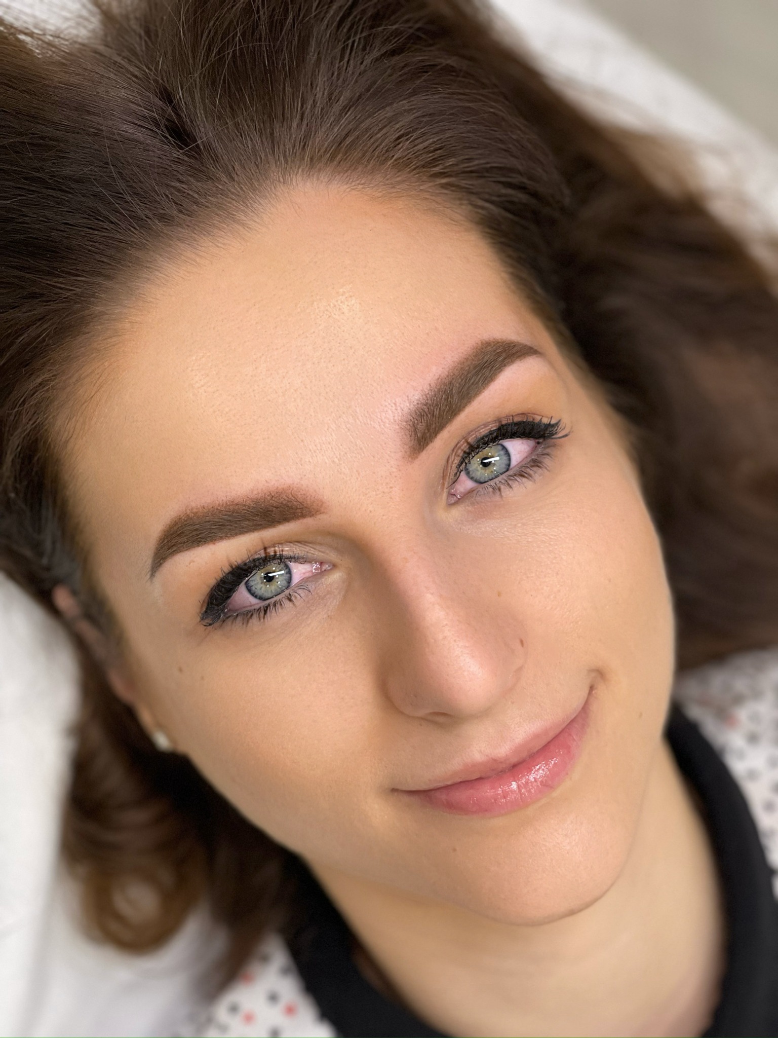 Portret kobiety z wyraźnie podkreślonymi brwiami i delikatnym makijażem oczu, wykonany z bliska w naturalnym świetle.