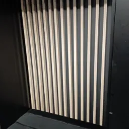 Drewniane lamele dekoracyjne na czarnej ścianie, tworzące nowoczesny element wykończenia wnętrza.