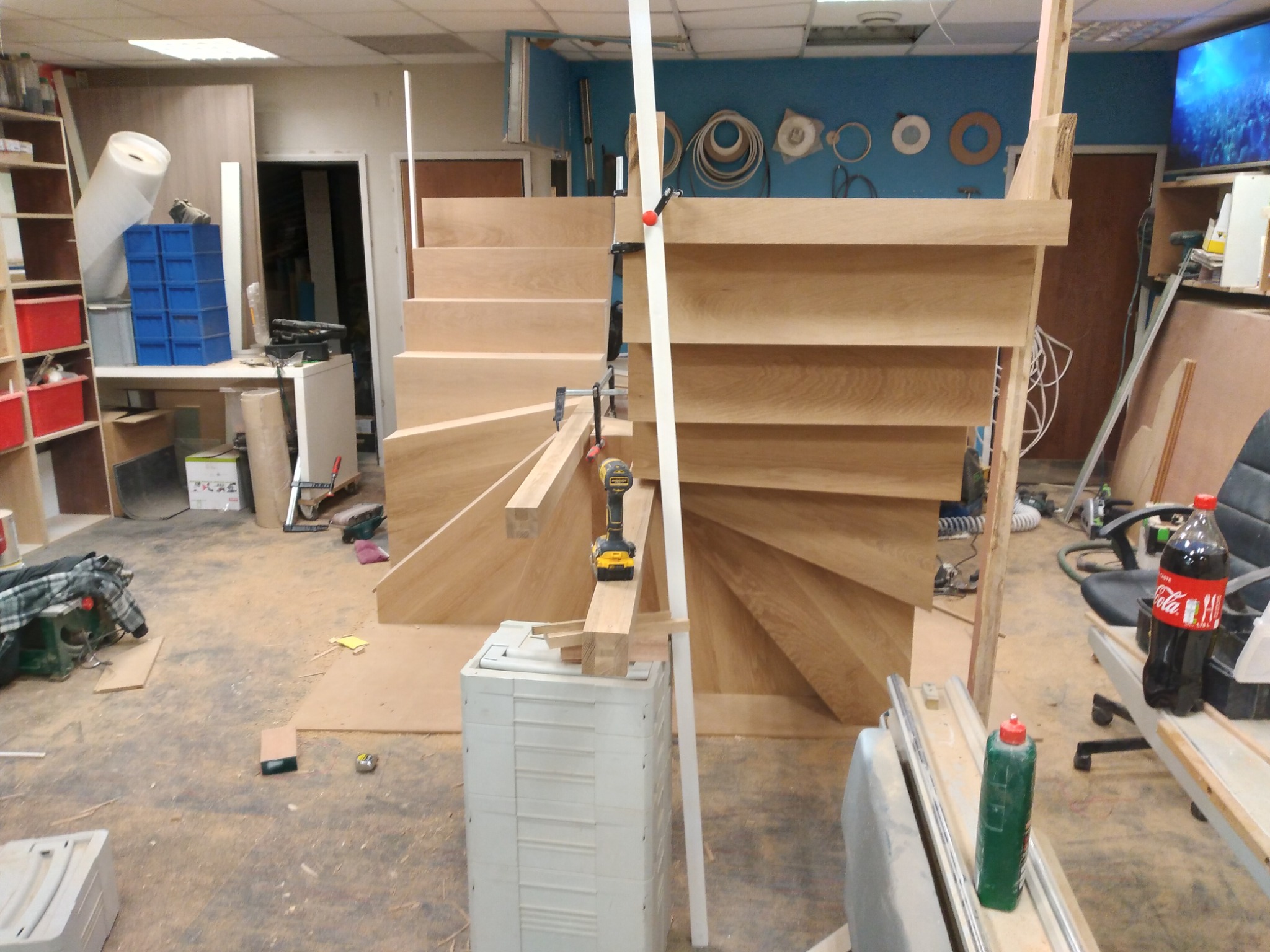 Konstrukcja drewnianych schodów spiralnych w trakcie montażu w warsztacie, widoczne narzędzia i elementy mocujące.