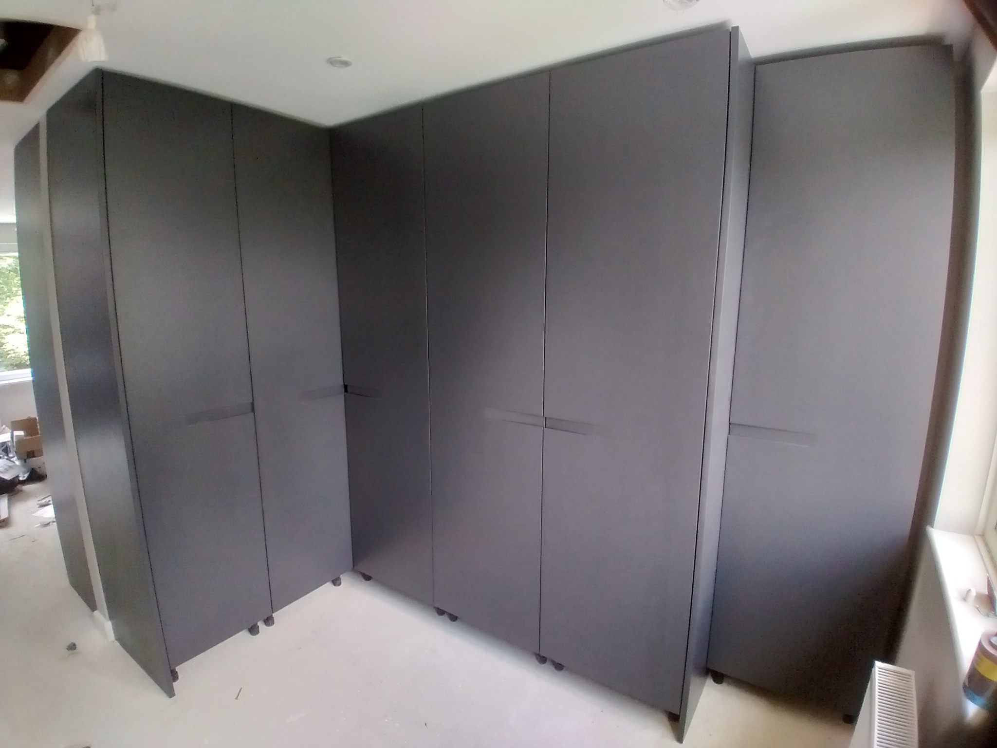 Szare szafy wnękowe z poziomymi uchwytami, zamontowane na kółkach, widoczne ślady po remoncie na podłodze.