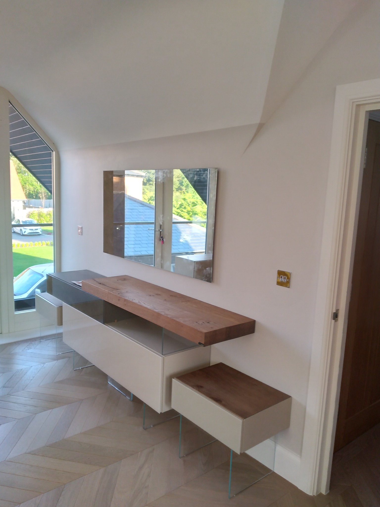 Nowoczesna konsola z blatem z litego drewna i lustrem, zamontowana w przedpokoju w Bylewie, z podłogą ułożoną w jodełkę.