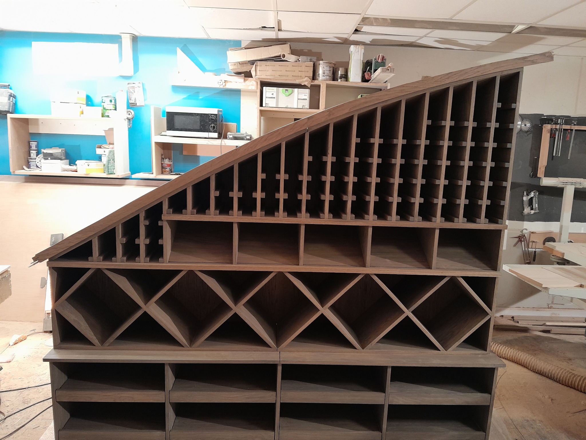 Drewniany regał o nietypowej konstrukcji z licznymi przegródkami, w trakcie budowy w warsztacie, widoczne narzędzia i materiały w tle.