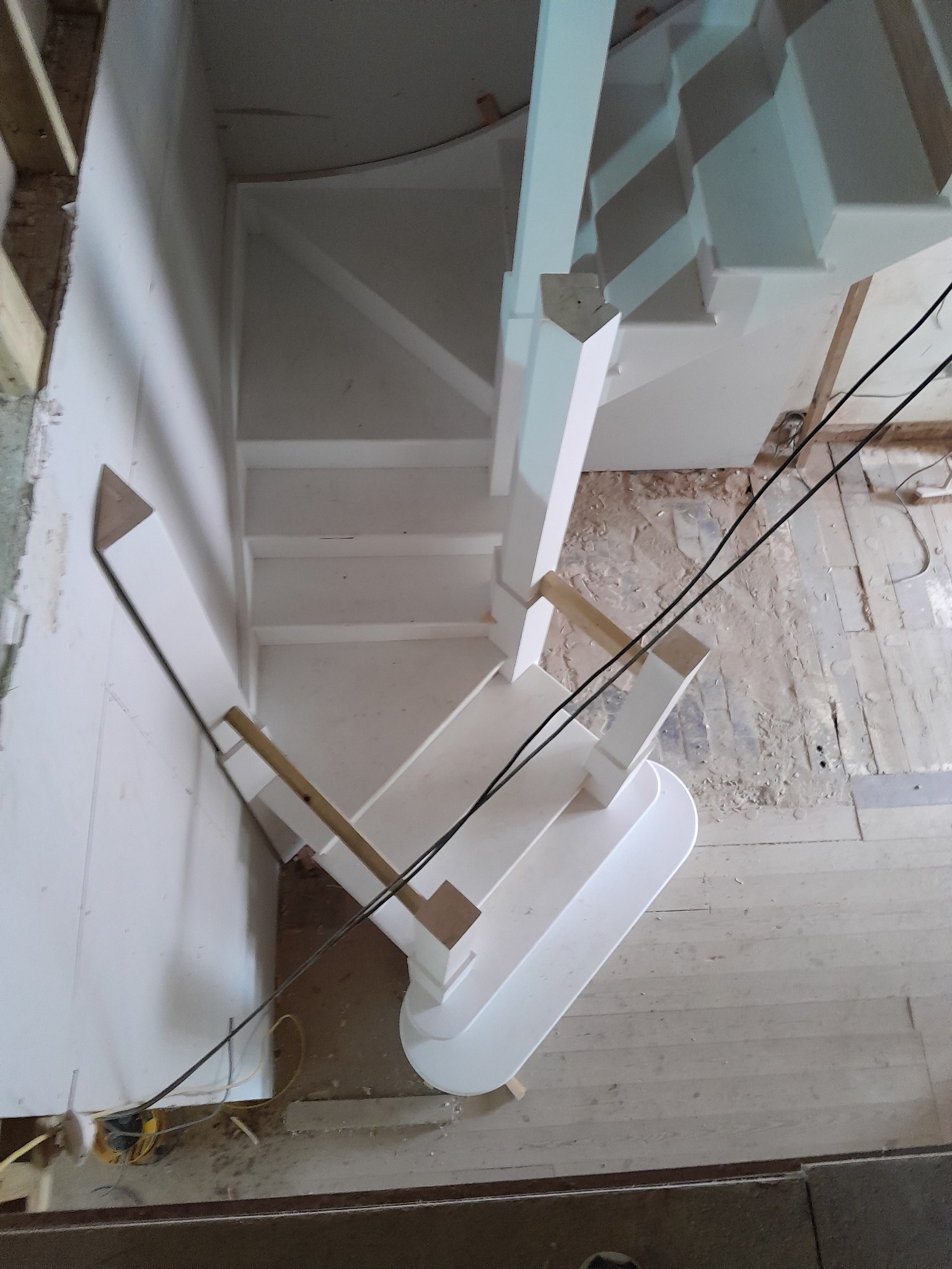 Widok z góry na białe schody drewniane w trakcie montażu, z widocznymi elementami konstrukcyjnymi i surową podłogą.