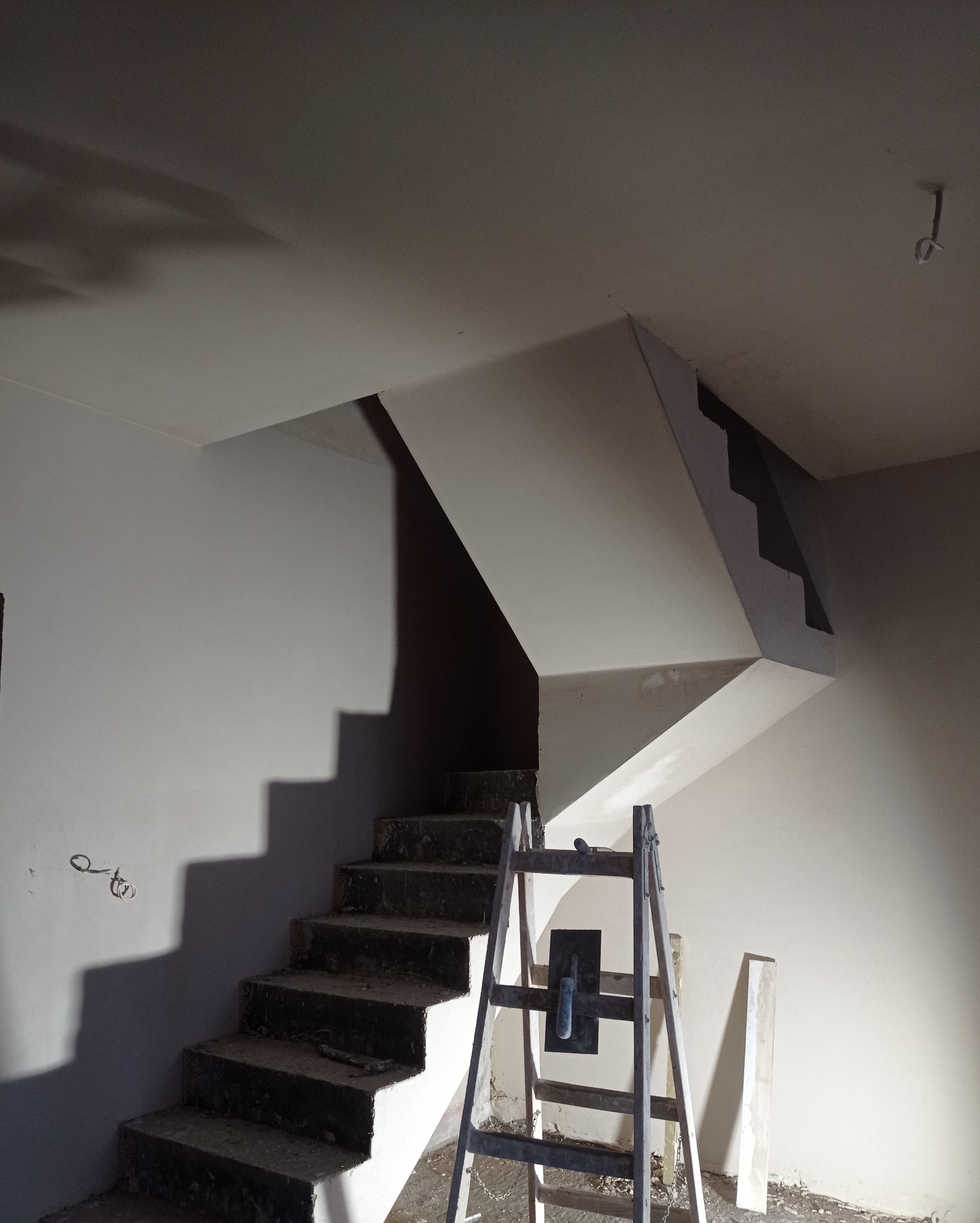 Świeżo położone gładzie gipsowe na klatce schodowej w Robakowie. Widoczne narzędzia i drabina malarska. Jasne, jednolite ściany.