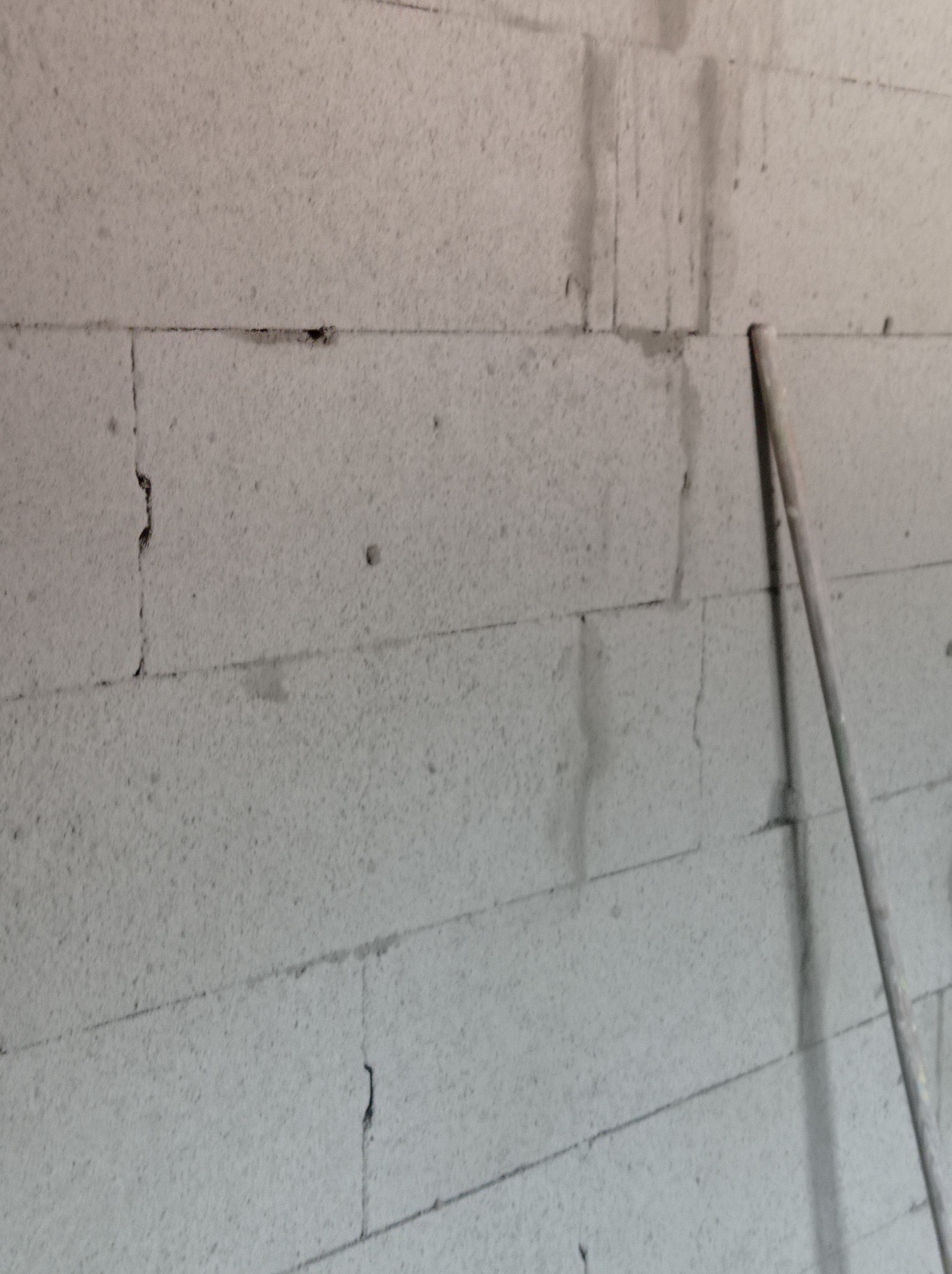 Ściana z bloczków z betonu komórkowego, widoczne ślady zaprawy i niedokładności w spoinach, fragment rusztowania w prawym górnym rogu.