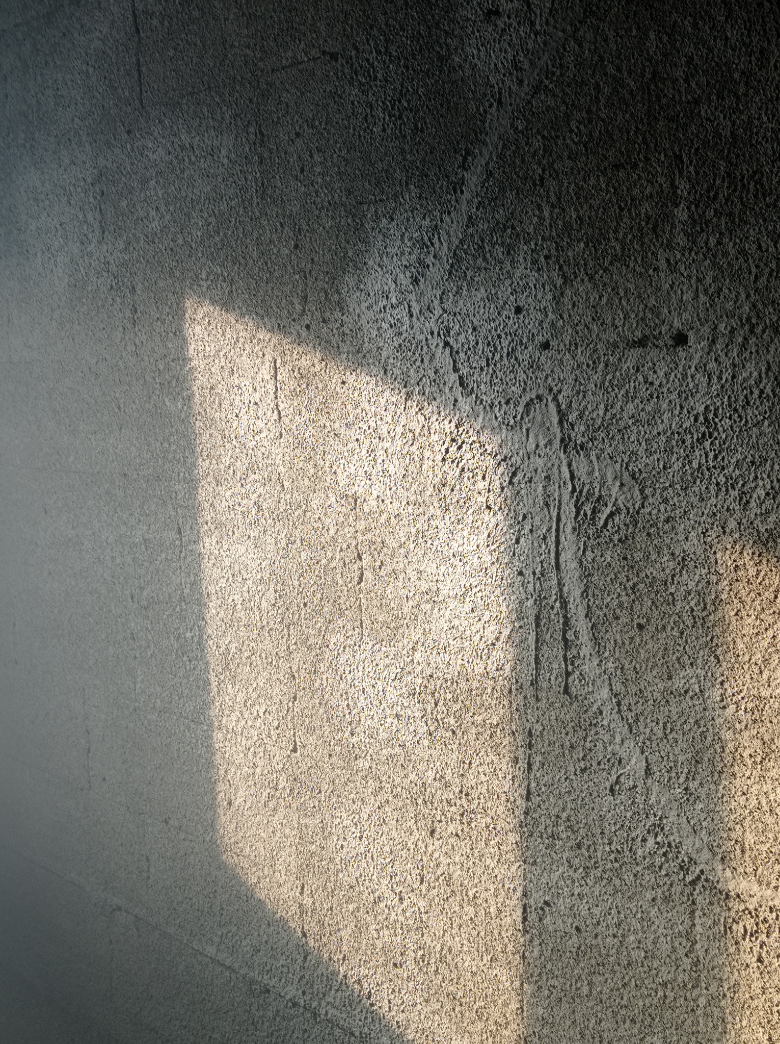 Szara ściana z tynkiem maszynowym oświetlona kwadratowym promieniem słońca, ukazującym fakturę.