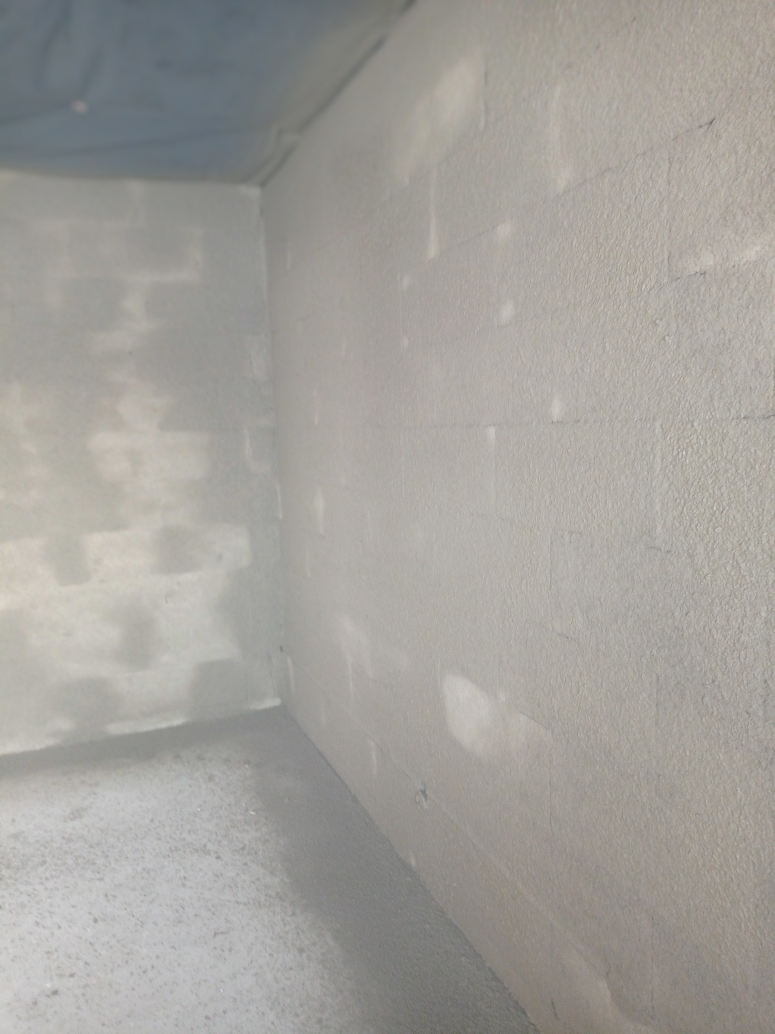 Wnętrze pomieszczenia w Kórniku po nałożeniu świeżych, jasnoszarych wypraw tynkarskich, widoczna struktura tynku na ścianach i podłodze.