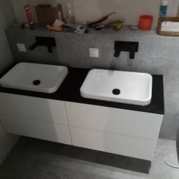 Adam Baczmański - Nowoczesna łazienka we Wrocławiu z podwójną białą umywalką nablatową na szafce z białymi frontami, czarnym blatem i wiszącą toaletą.